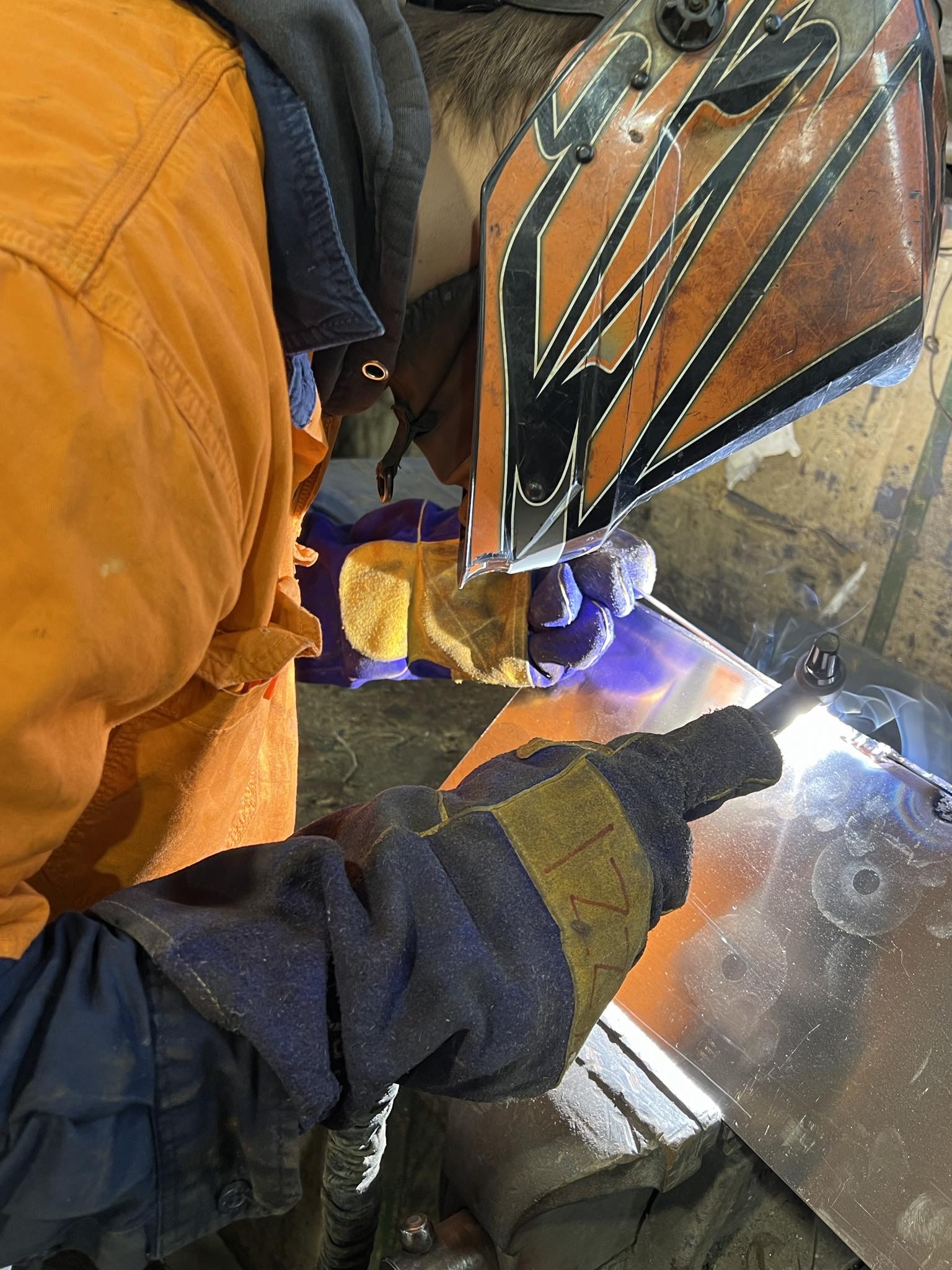 Close up view of young man in welding mask working on metal casing for time capsule.  