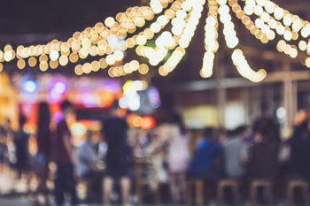 Blurred image of people outside at an event at night with party lights shining above